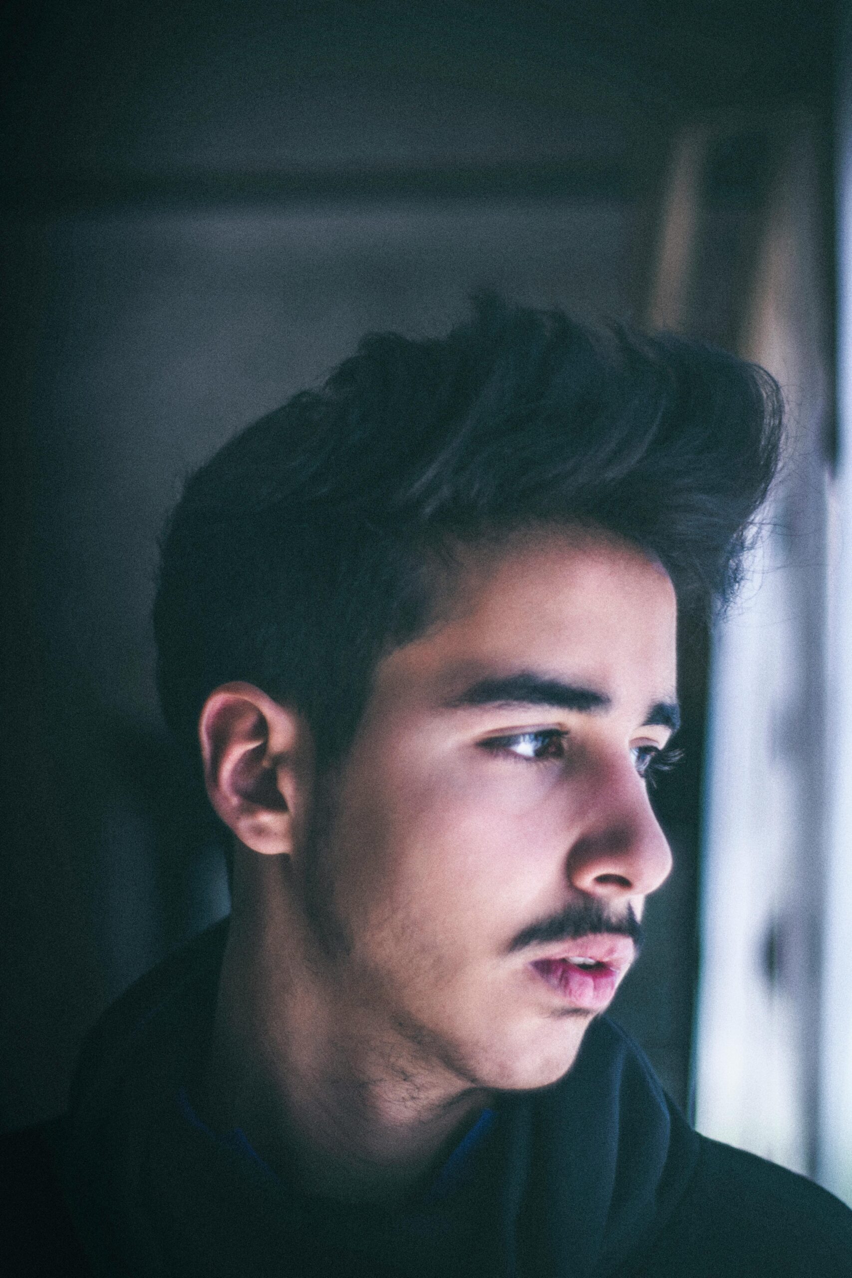 Side profile portrait of a young man looking thoughtfully out a window with soft lighting.